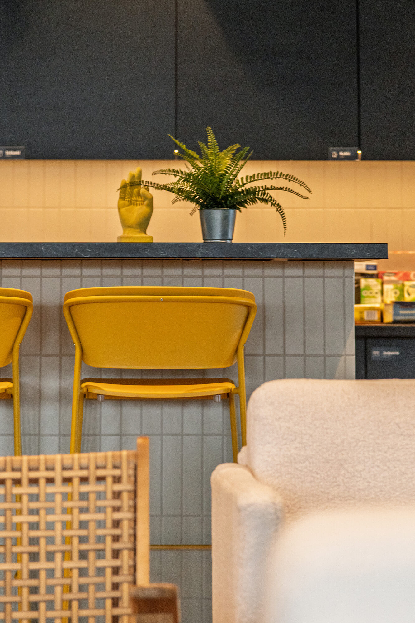 Żółte krzesła barowe przy blacie z rośliną i złotą rzeźbą dłoni. Nowoczesne wnętrze.