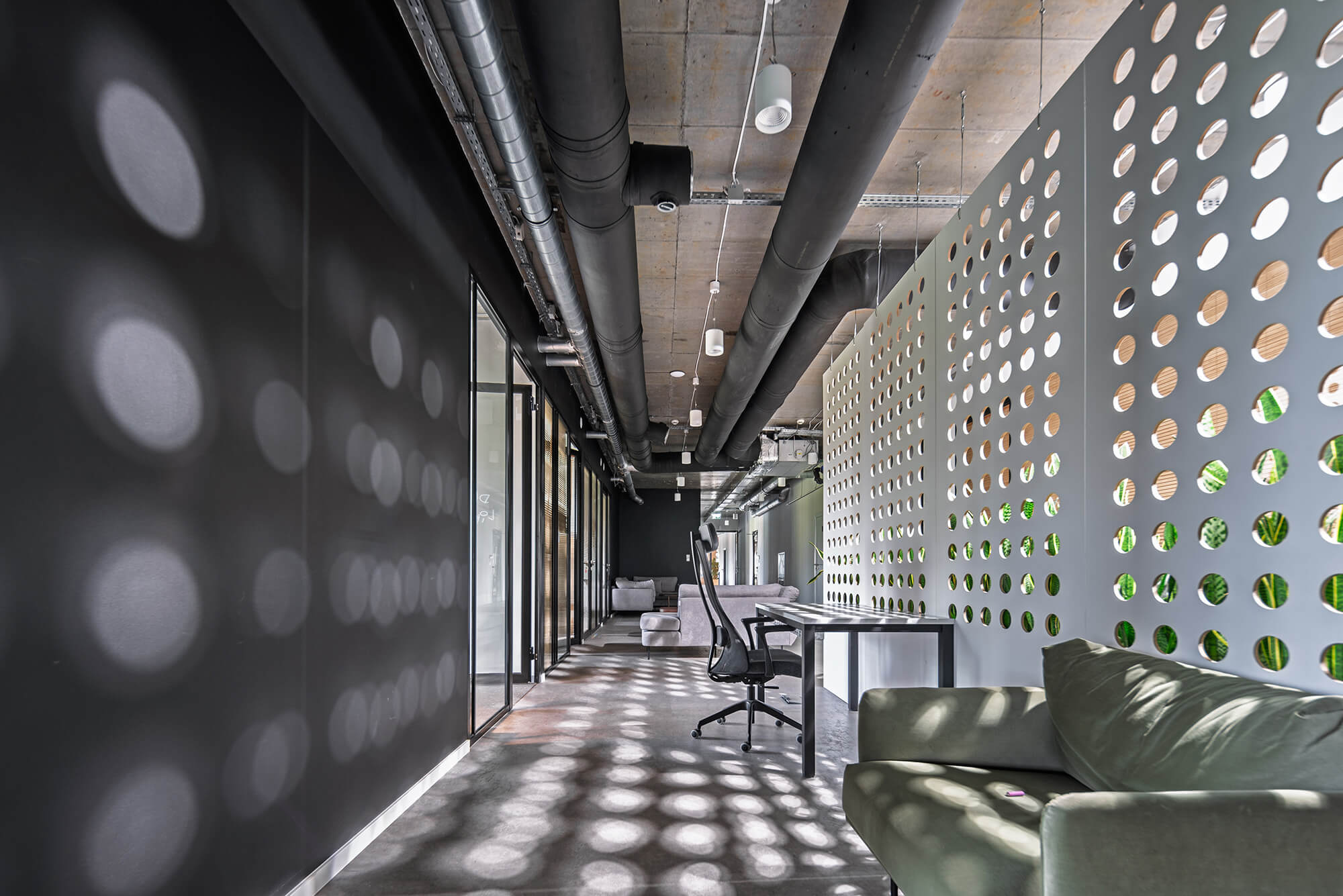 Nowoczesne biuro z betonowym sufitem, czarnymi rurami i ścianką działową z okrągłymi otworami.