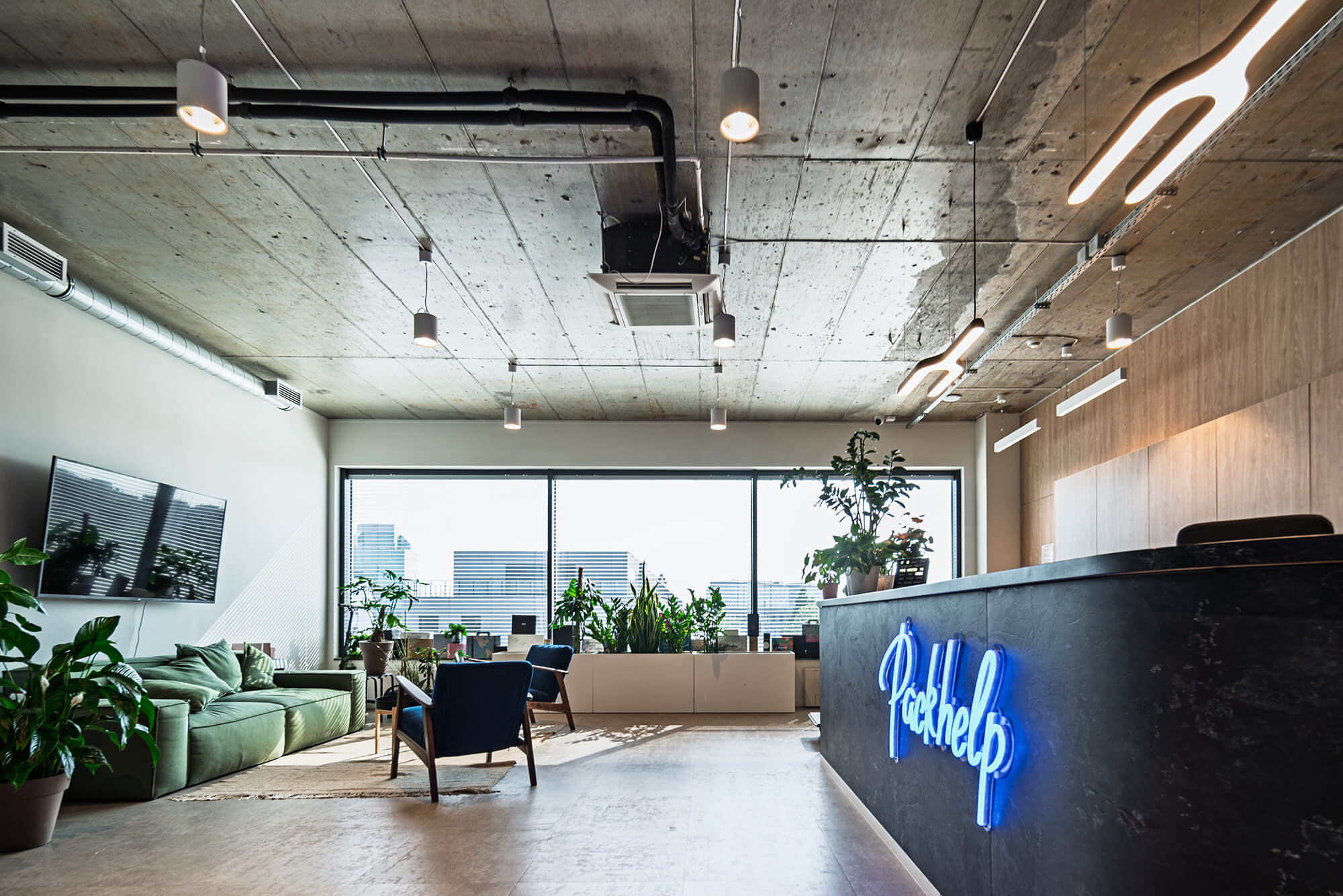 Nowoczesne biuro z recepcją Packhelp, zieloną sofą i roślinami.