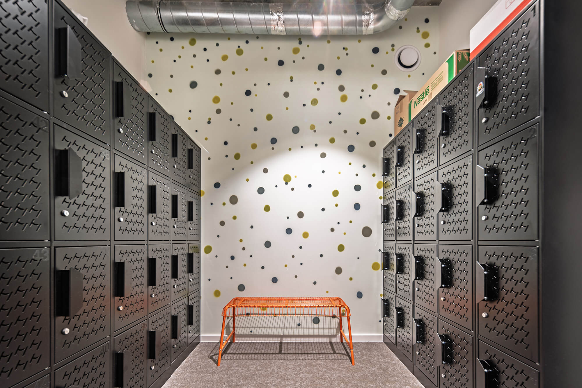 Szatnia z czarnymi szafkami, ścianą w kropki i pomarańczową ławką