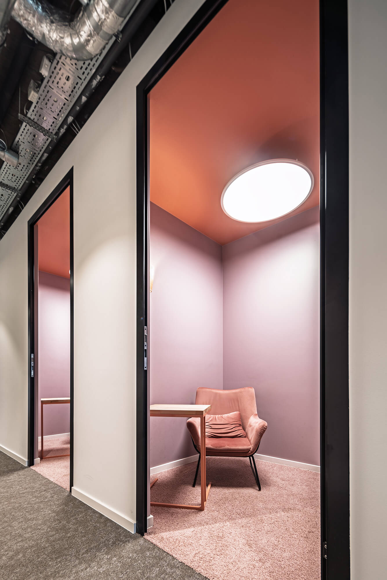 Różowy fotel w nowoczesnej kabinie biurowej z oświetleniem sufitowym.