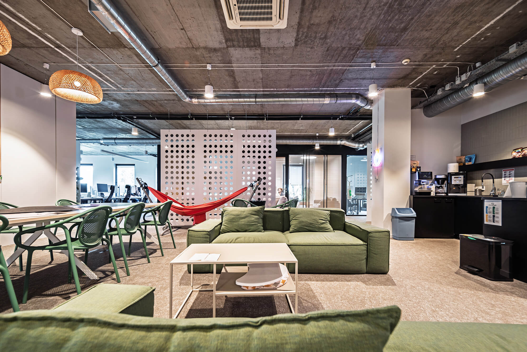 Nowoczesne biuro z zieloną sofą, hamakiem i stołami. Otwarta przestrzeń biurowa.