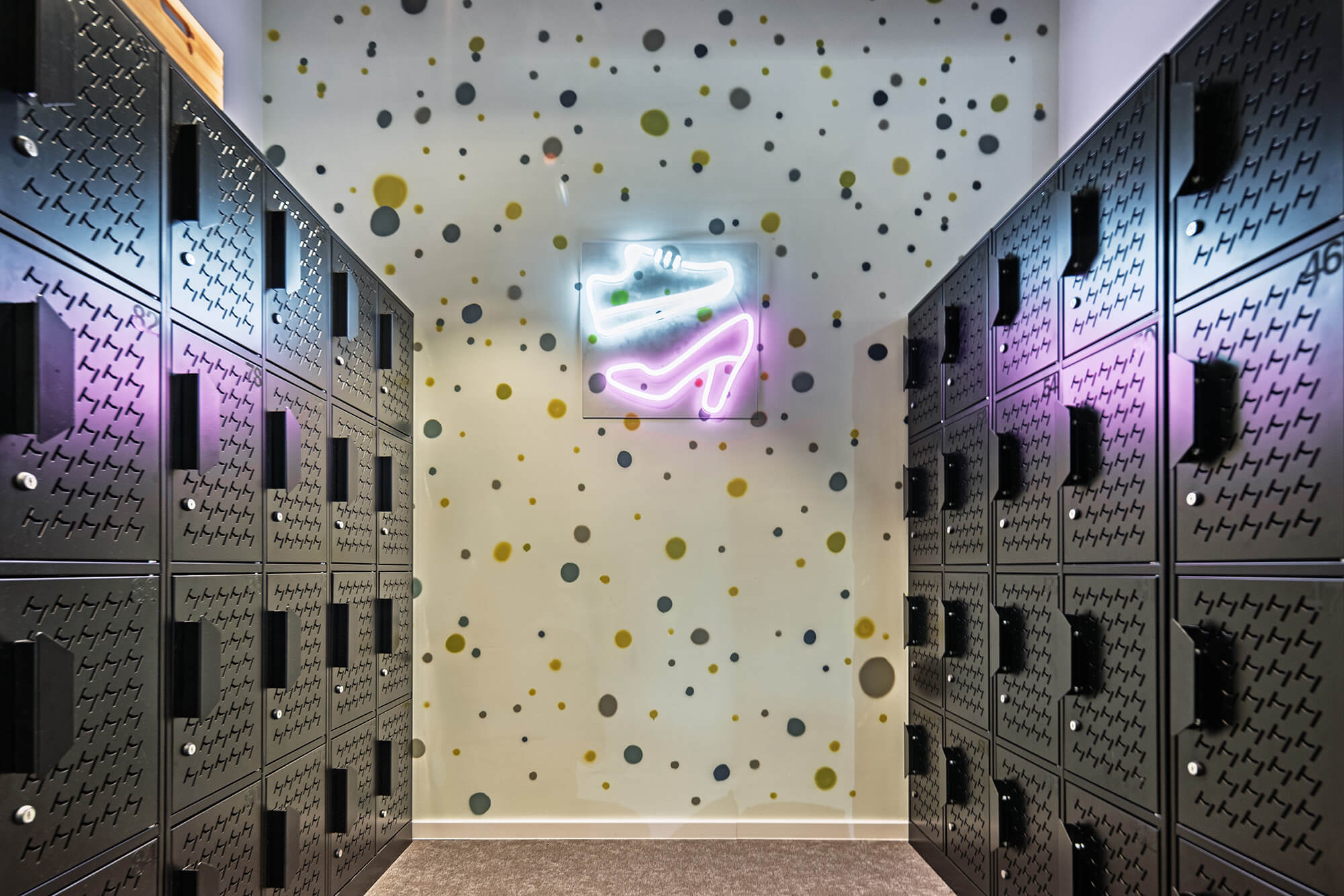 Szatnia z neonowym znakiem buta na obcasie i wzorem w kropki na ścianie.
