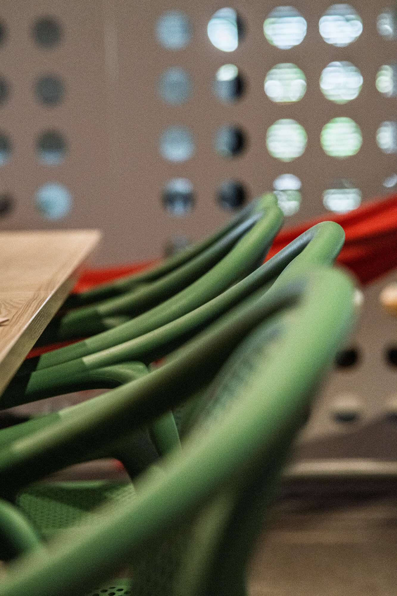 Zielone krzesła przy drewnianym stole na tle dekoracyjnej ściany z otworami.