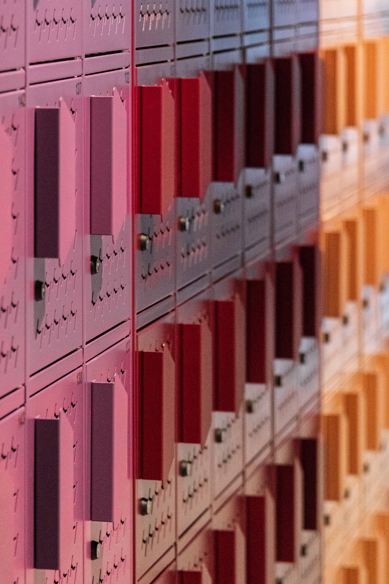 Kolorowe skrytki pocztowe w rzędach, od różowych po pomarańczowe.