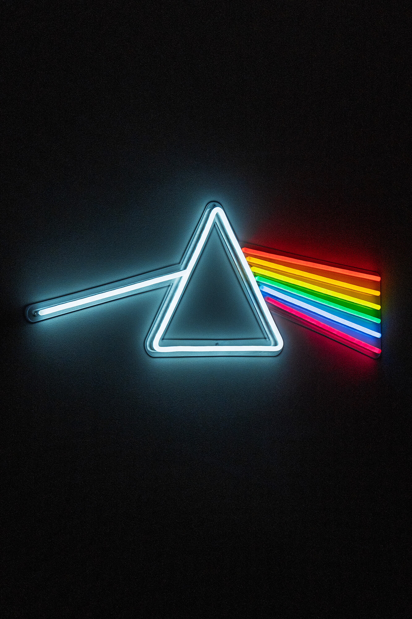 Neonowy pryzmat rozszczepiający światło na tęczę. Grafika nawiązująca do Dark Side of the Moon.