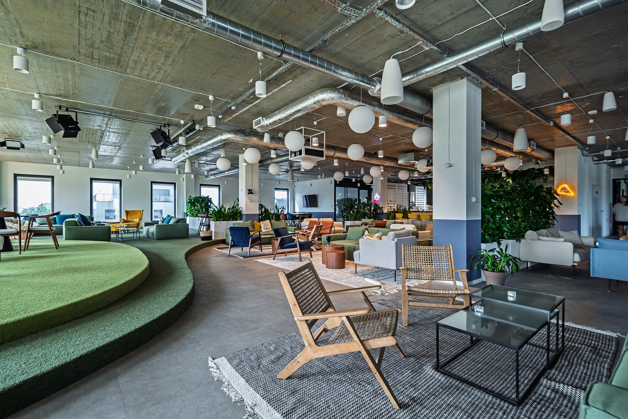 Widok na nowoczesną otwartą przestrzeń biurową z miejscami do siedzenia i zielenią.