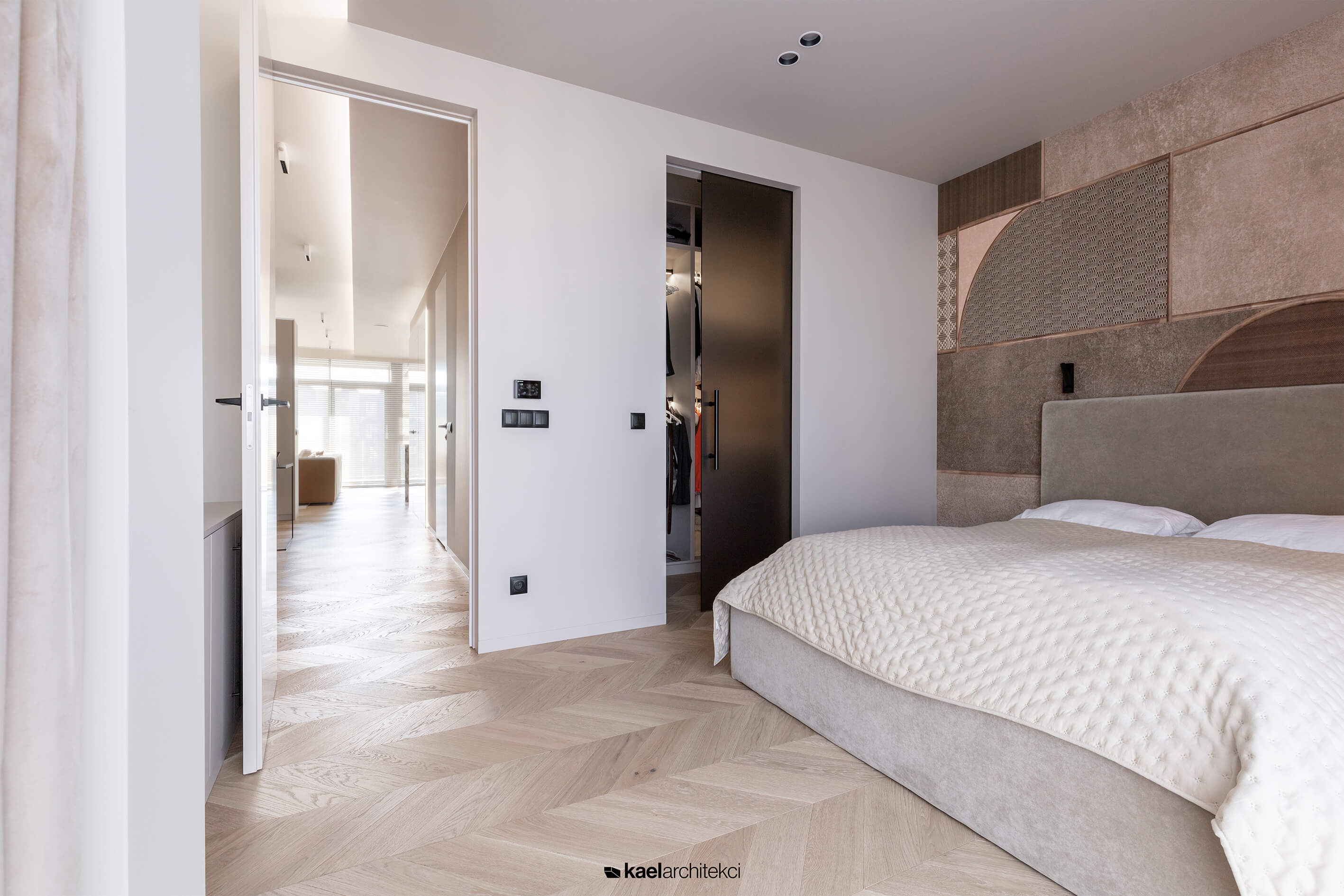 Elegancka sypialnia z parkietem w jodełkę, garderobą i dekoracyjną ścianą.